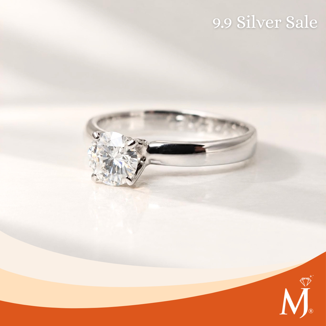 A silver solitaire engagement ring with a round brilliant-cut diamond, displayed on a white surface with a soft shadow. The image includes a '9.